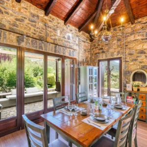 Stone dining room at Villa Mainalis with a set table and doors opening to the terrace