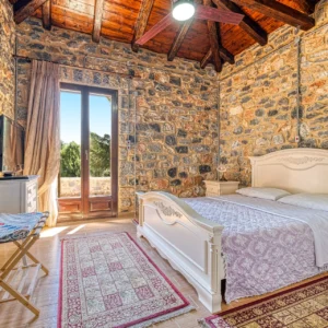 Double bedroom with exposed stone walls, timber ceiling and terrace access at Villa Mainalis