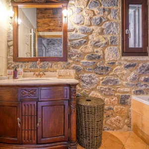 Bathroom with stone walls, wooden vanity and bathtub at Villa Mainalis